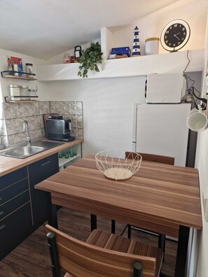 Une cuisine compacte avec une table en bois, un évier, une bouilloire et un four à micro-ondes.