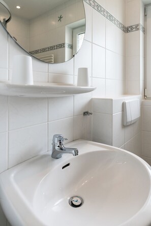 A white bathroom with a sink, mirror, and towel dispenser. - Comfortable house Jule with garden, terrace, WLAN and private parking in Tinnum (Tinnum)