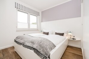 A bedroom with a bed, a nightstand, a lamp, a window with blinds, and a view of the outside. - Comfortable house Jule with garden, terrace, WLAN and private parking in Tinnum (Tinnum)