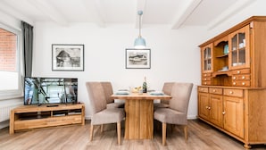 Ein Essbereich mit einem Holztisch, zwei Stühlen, einem Holzschrank und einem Fernseher auf einem Schrank.