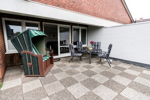 A patio with a checkered floor, a wicker chair, a table with chairs, and a sliding glass door leading to a room. - Comfortable house Jule with garden, terrace, WLAN and private parking in Tinnum (Tinnum)