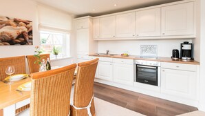A modern kitchen with white cabinets, a wooden countertop, and a dining area with wicker chairs. - Comfortable vacation apartment with balcony and modern furnishings in Westerland (Westerland)