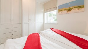 A bedroom with a bed, white wardrobe, and a painting of a beach scene. - Comfortable vacation apartment with balcony and modern furnishings in Westerland (Westerland)