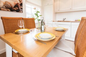 A dining table set with plates, glasses, and cutlery in a bright kitchen with white cabinets and wicker chairs. - Comfortable vacation apartment with balcony and modern furnishings in Westerland (Westerland)