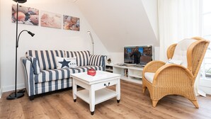 A cozy living room with a striped sofa, a wicker chair, a white coffee table, and a television on a white stand. - Comfortable vacation apartment with balcony and modern furnishings in Westerland (Westerland)