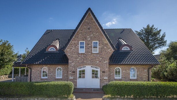 A two-story brick house with a symmetrical facade, a central entrance with a white door, and a peaked roof. - Comfortable vacation apartment with balcony and modern furnishings in Westerland (Westerland)