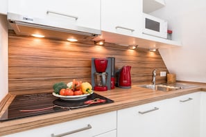 Eine moderne Küche mit integriertem Induktionskochfeld, einer roten Kaffeemaschine und einer Mikrowelle in einem weißen Schrank.