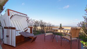 A patio with a white outdoor seating area, including a cushioned chair and a table with a bowl and pineapple. - Beautiful 3-room apartment with direct view of the mudflats in Rantum (Rantum)