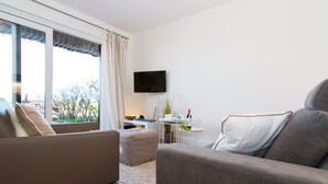 A modern living room with a sofa, a small table, and a TV mounted on the wall. - Beautiful 3-room apartment with direct view of the mudflats in Rantum (Rantum)