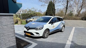 Une voiture blanche est garée dans un parking couvert, avec un chemin piétonnier dallé.