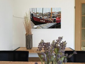 A dining table with a vase of dried plants, a framed photograph of boats, and a wooden door. - Park Brekkense Wiel 044 (Lemmer)