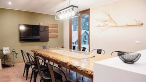 A dining area with a long wooden table, black chairs, a television mounted on the wall, and a window with a view of houses. - w Calm 4BR Villa w Fireplace in Sacred Valley (Calca)