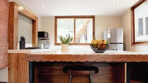 Eine Küche mit einer Holzinsel, Barhocker, einem Kühlschrank und einem Fenster mit Blick auf eine Holzterrasse.