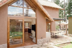A modern house with large glass doors leading to a living area, a stone patio, and a TV mounted on the wall. - w Impressive 2BR Villa in Sacred Valley (Calca)
