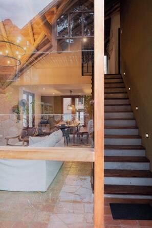 Un interior amplio con una escalera que conduce a un nivel superior, una zona de estar con sofá y sillones, y una mesa de comedor.