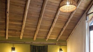Une chambre avec un plafond en bois, un lit recouvert de draps blancs, deux lampes de chevet et une grande fenêtre.