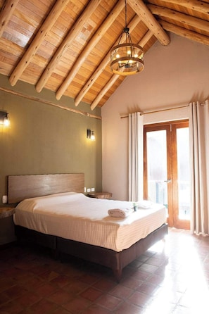 A bedroom with a wooden ceiling, a bed with a headboard, a nightstand, a wall-mounted light, and a window with curtains. - w Warm 3BR Villa in Sacred Valley (Calca)