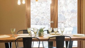 Ein Esstisch für sechs Personen, gedeckt mit Kristallgläsern und Tellern, mit einem kleinen Pflanzenarrangement als Mittelstück und einer Holzbalkendecke mit Pendelleuchten.