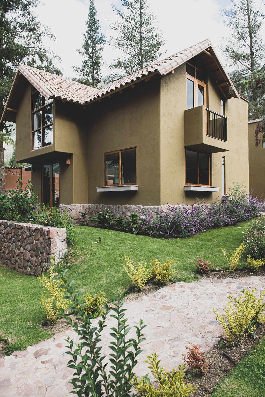 A two-story house with a stone foundation, a flat roof, and a balcony on the second floor.