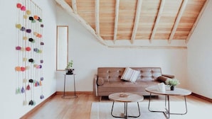 Una habitación tipo loft con techo de madera, un sofá de cuero marrón, dos mesas redondas y una decoración pomposa y colorida en la pared.