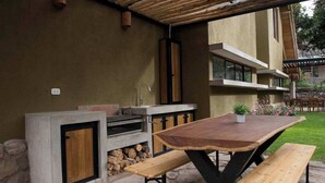 Cocina exterior con encimera de piedra, horno integrado y mesa de madera con bancos.
