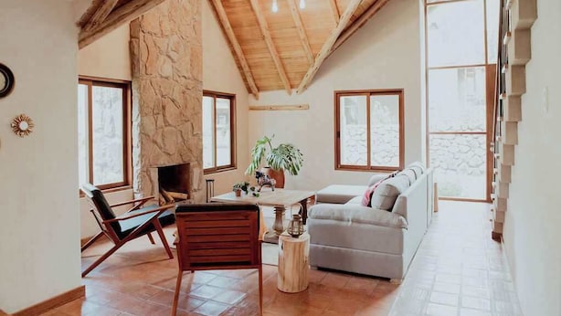 Un salón espacioso con chimenea de piedra, techo de madera y ventanas grandes.