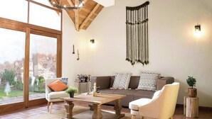 A cozy living room with a large window, a wooden coffee table, a sofa, and a hanging macrame wall decoration. - w Peaceful 2BR Riverside Villa in Sacred Valley (Calca)