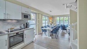 Une cuisine moderne avec des armoires blanches, un four encastré et un coin repas comprenant une table blanche et des chaises bleues.