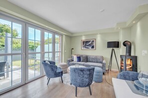 Ein geräumiges Wohnzimmer mit einem großen Schiebeglasfenster, das auf eine Terrasse führt, einer grauen Sofagarnitur und einem modernen Kamin.