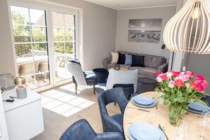 A dining area with a table set for four, a sofa, and a large window with a view of the outdoors. - Exclusive thatched house in Wenningstedt with sauna, garden and modern furnishings (Wenningstedt)