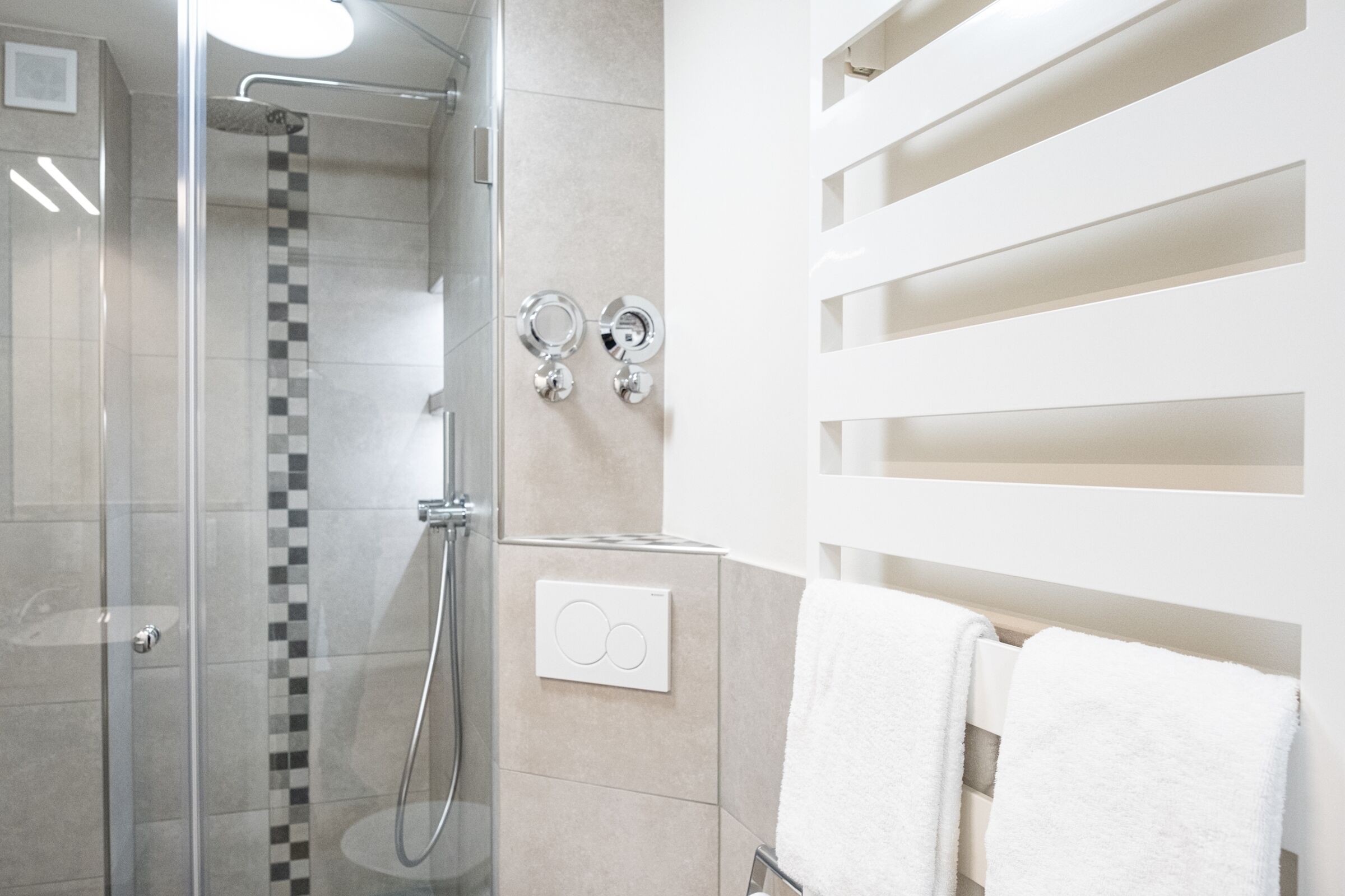 Une salle de bain moderne dotée d’une douche à parois de verre, d’un pare-chocs en carreaux, d’un porte-serviettes et d’un panneau de commande fixé au mur.