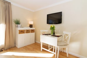 A dining area with a white table set for two, a television mounted on the wall, and a cabinet with wooden crates. - Comfortable apartment with balcony in Westerland (Westerland)