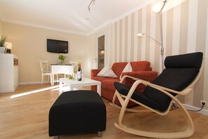 A modern living room with a sofa, a rocking chair, a coffee table, and a television mounted on the wall. - Comfortable apartment with balcony in Westerland (Westerland)