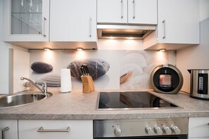 A modern kitchen with a stainless steel sink, an induction cooktop, and white cabinets. - Modern apartment with balcony and comfortable furnishings in Westerland (Westerland)