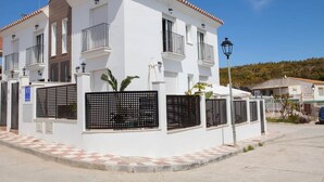 Un edificio residencial blanco de dos pisos con balcones, entrada protegida por una reja y un farol.