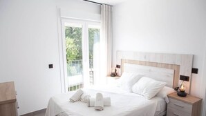 Un dormitorio moderno con una cama grande, cabecera de madera, dos mesitas de noche con lámparas y vistas a zonas verdes por la ventana.