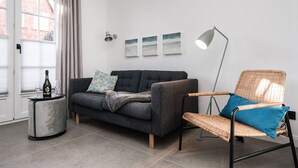 A modern living room with a grey sofa, a wicker chair, a round side table with a bottle and glasses, and a floor lamp. - Haus Friesenperle: Comfortable vacation home with terrace and garden in Westerland (Westerland)
