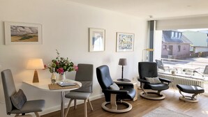 En moderne stue med udsigt til gaden, med et rundt bord, to lænestole, en sofa og et sofabord.