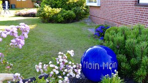 Un jardí amb un senyal blau esfèric que diu “Moin Moin”, envoltat de diverses plantes i flors.