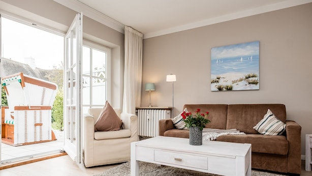 En stue med en beige sofa, et hvidt sofabord og et maleri af en strand.