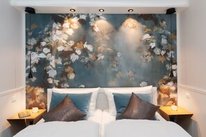 Een slaapkamer met bloemen behang, een wit bed en twee nachtkastjes met lampen.