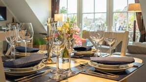 A dining table set with wine glasses, plates, and cutlery, with a vase of flowers in the center. - Beautiful vacation apartment with sauna, indoor pool and fitness room in Keitum (Keitum)