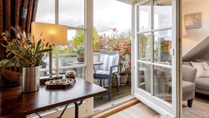 A cozy room with a wooden table, a lamp, and a view of the garden through large windows. - Beautiful vacation apartment with sauna, indoor pool and fitness room in Keitum (Keitum)