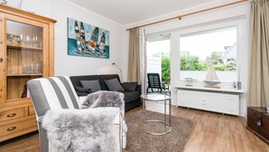 En stue med sofa, lænestol og et bord med lampe. Der er et maleri på væggen og et vindue med gardiner.