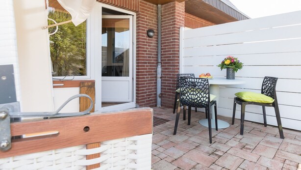 En udendørs terrasse med et bord og stole, et hvidt hegn og en murstensmur.