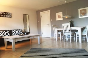 Ein Wohnzimmer mit einem weißen Sofa, einem weißen Couchtisch, einem Esstisch mit weißen Stühlen, einem schwarz-weißen Teppich und einer weißen Tür.