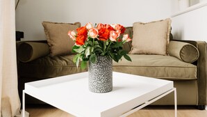 Ein weißer Tisch mit einer dekorativen Vase mit Blumen, vor einer beige farbenen Couch mit Kissen.