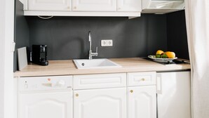 Eine moderne Küche mit weißen Schränken, einer schwarzen Spritzschutzwand, einem Spülbecken, einer Kaffeemaschine und einer Obstschale.