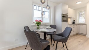 A modern kitchen with white cabinets, a dining table with four grey chairs, and pendant lights above. - This beautiful and new end terraced house is centrally located in Westerland (Westerland)