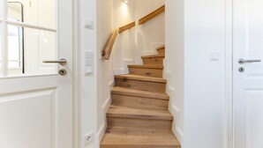 A wooden staircase with white walls and a door on the left. - This beautiful and new end terraced house is centrally located in Westerland (Westerland)